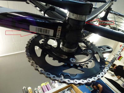 The serial number is printed on a white sticker and embossed on the underside of the bicycle frame near the pedals.